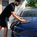 ACP11389 - Man using a gray Spigen microfiber towel to dry the hood of a wet blue car in a driveway