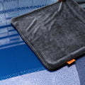 ACP11389 - Hand holding up the corner of a gray Spigen microfiber towel over a wet, water-splashed surface